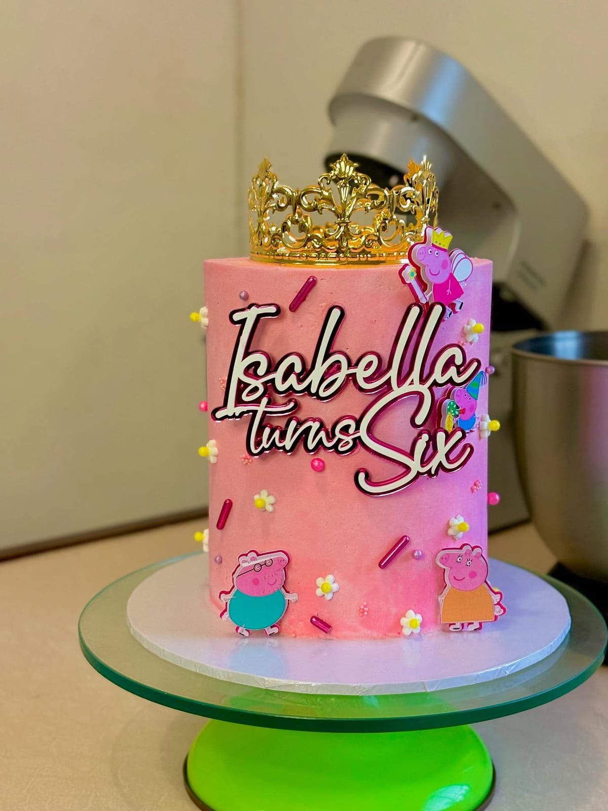 Soft pink birthday cake with a gold crown and the name Isabella piped across the front